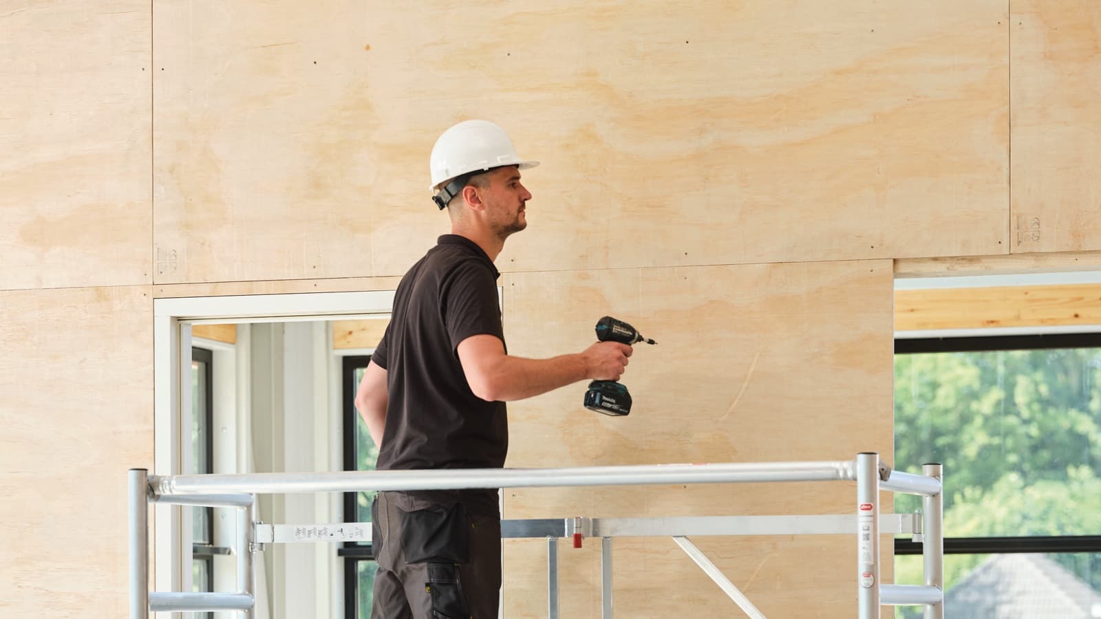 Werker op een kamersteiger in een woning in aanbouw